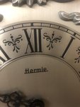 Nástěnné hodiny, vyrobeny  německou firmou  Hermle. Elegantní ciferník, kolem něhož jsou okrasné motivy. 